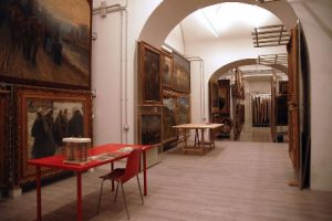 Qui sopra, il deposito quadri di Palazzo reale. In alto, una panoramica della piazza del Plebisciro con la reggia napoletana dove si trova anche la biblioteca nazionale