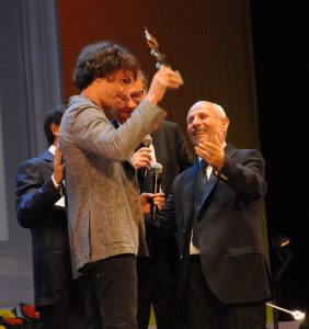 Qui sopra, Jorit con Giuseppe Leone al premio Penisola sorrentina. In alto, due delle sue opere